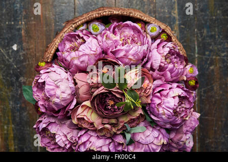 Panier plein de pivoines rose et violet , bourgogne , panier avec poignée est sur le plancher en bois, vue du dessus Banque D'Images