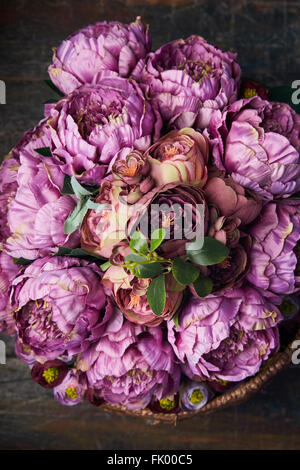 Panier plein de pivoines rose et violet , bourgogne , panier avec poignée est sur le plancher en bois, vue du dessus Banque D'Images