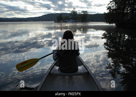 Jeune fille de canots sur un lac reflétant les nuages que le soleil se lève sur une colline. Banque D'Images