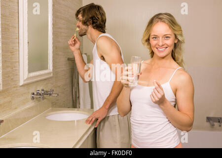 Femme blonde en prenant un comprimé avec son petit ami se brosser les dents Banque D'Images