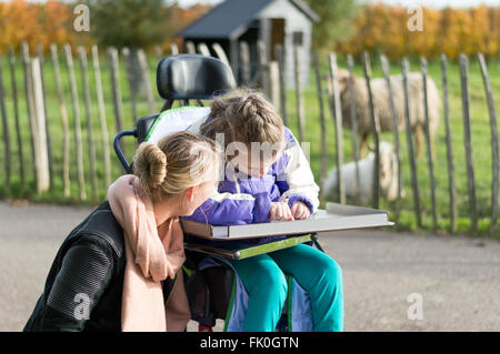 Un enfant handicapé dans un fauteuil roulant qui sont pris en charge par un travailleur bénévole Banque D'Images