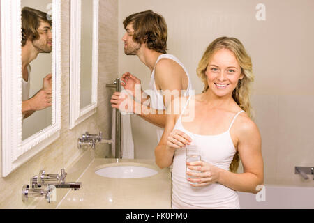 Femme blonde en prenant un comprimé avec son petit ami se brosser les dents Banque D'Images