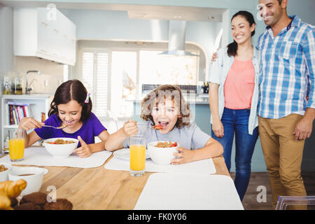 Petit-déjeuner tout en ayant des enfants heureux parents debout par table Banque D'Images