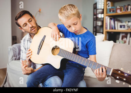 L'enseignement du père fils à jouer de la guitare, assise sur un canapé Banque D'Images