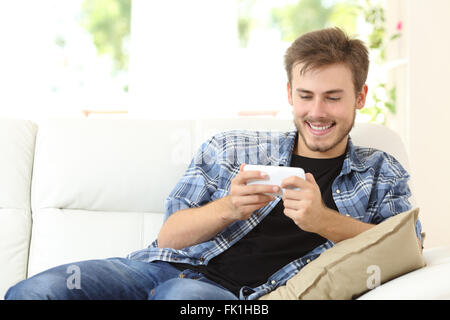 Homme jouant les jeux en ligne avec un téléphone intelligent assis sur un canapé à la maison Banque D'Images