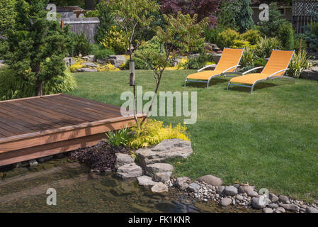 Une paire de chaises de designer jaune vif vous invite à vous détendre dans ce jardin joliment aménagé avec terrasse couvrant une cr Banque D'Images