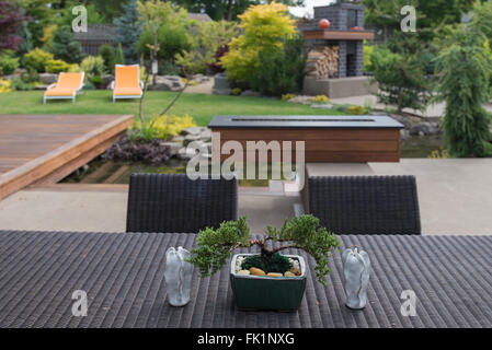 Un petit bonsaï est assis sur une table de patio d'arrière-cour contemporaine entre deux bougies sculptées en relief. Banque D'Images