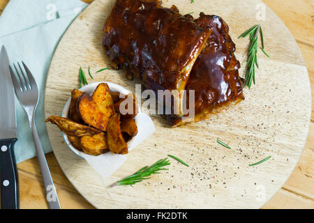 Vue du dessus montrant rack de ribs barbecue fumé avec sauce, les quartiers de pommes de terre et épices sur un plateau en bois Banque D'Images