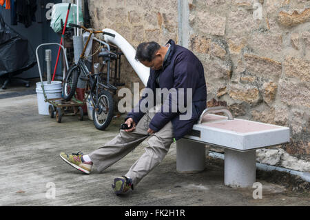 Middle aged man sleeping chinois alors qu'il était assis sur un banc. Stanley, Hong Kong, Chine. Banque D'Images