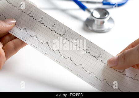 Mains tenant un ECG normal avec un stéthoscope dans l'arrière-plan Banque D'Images