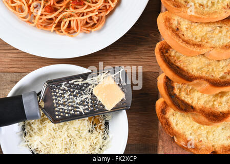 Vue de dessus de l'ail du pain sur une planche à découper et un plat de spaghetti avec une râpe à fromage avec du fromage parmesan râpé. Banque D'Images