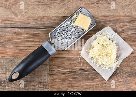 Râpe à fromage parmesan et sur une table de cuisine en bois. Certains fromage râpé est sur un morceau de papier parchemin à côté de la râpe. Haut Banque D'Images