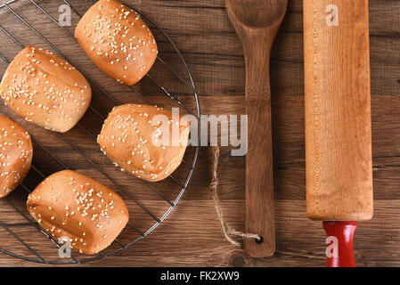 Vue aérienne d'un rack de petits pains aux graines de sésame à côté d'une spatule en bois et un rouleau à pâtisserie. Banque D'Images