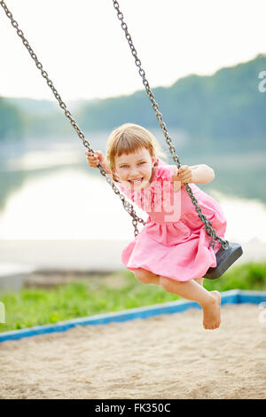 Happy girl swinging sur swing en été, sur une aire de jeux Banque D'Images