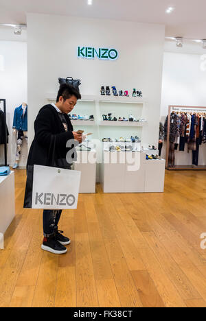 Paris, France, acheteur chinois, Man Designer vêtements Label Shops marques Shopping, Acheteur utilisant iPhone, à l'intérieur de 'la Vallée Village', Discount Mall, Marne-la Vallée, Kenzo Shop, tenant le sac de shopping Banque D'Images