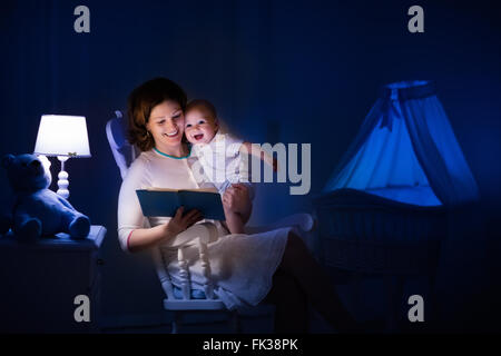 La mère et l'enfant de lire un livre dans une chambre sombre. Maman et enfant à lire les livres avant de le mettre au lit. Famille dans la soirée. Banque D'Images