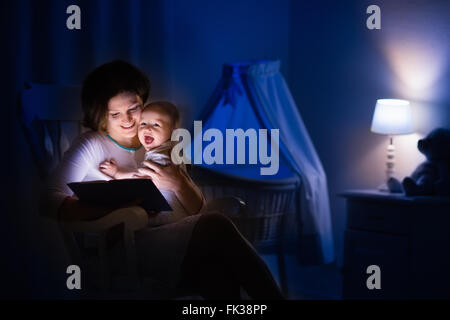 La mère et l'enfant de lire un livre dans une chambre sombre. Maman et enfant à lire les livres avant de le mettre au lit. Famille dans la soirée. Banque D'Images