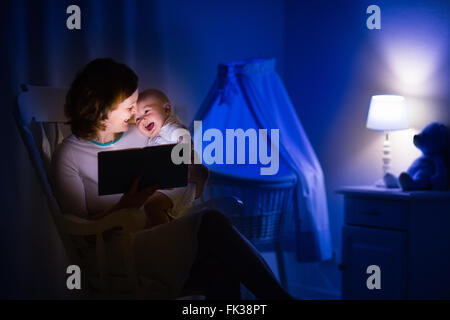 La mère et l'enfant de lire un livre dans une chambre sombre. Maman et enfant à lire les livres avant de le mettre au lit. Famille dans la soirée. Banque D'Images