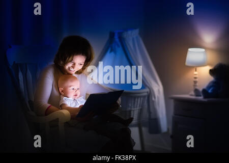 La mère et l'enfant de lire un livre dans une chambre sombre. Maman et enfant à lire les livres avant de le mettre au lit. Famille dans la soirée. Banque D'Images