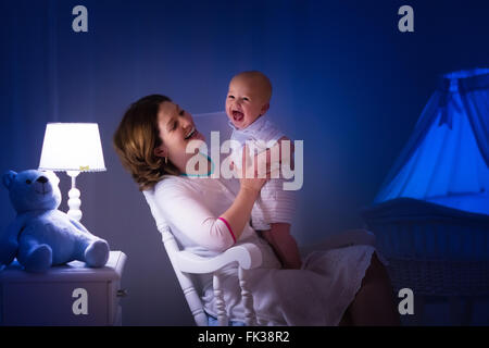 La mère et l'enfant de lire un livre dans une chambre sombre. Maman et enfant à lire les livres avant de le mettre au lit. Famille dans la soirée. Banque D'Images