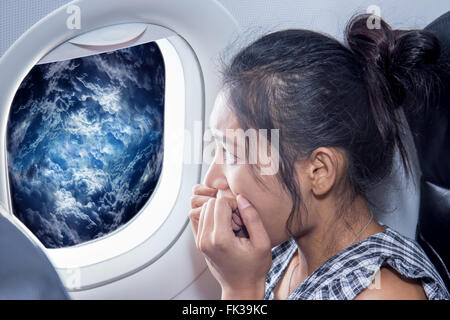 Peur femme regarde les nuages à partir de la fenêtre d'un avion Banque D'Images