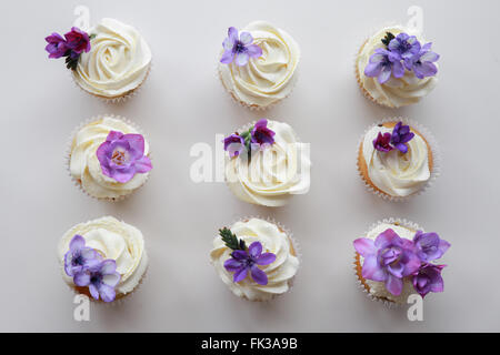 Des fleurs de freesia violet sur la vanille cupcakes avec glaçage à la crème fouettée Banque D'Images