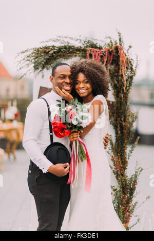 Happy black newlyweds smiling et serrant sur le toit pendant leur cérémonie de mariage Banque D'Images