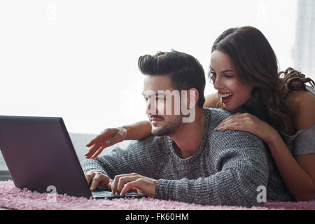 Jeune couple avec coffre allongé sur un tapis, la technologie wi-fi Banque D'Images