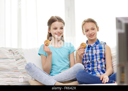 Happy girls watching TV and eating cookies à la maison Banque D'Images