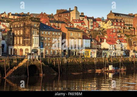 Maisons en rangée, de bars et restaurants sur Pier Road, côté ouest de la rivière Esk, éclairé par un faible soleil en hiver, Whitby, North Yorkshire Banque D'Images