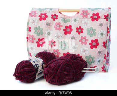 Tricot à motifs fleurs rose / artisanat sac avec des aiguilles à tricoter, et deux pelotes de laine de couleur bourgogne sur un fond blanc. Banque D'Images