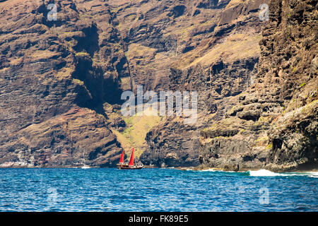 Bateau à voile avec voiles rouge devant les falaises de Los Gigantes, Santiago del Teide, Tenerife, Canaries, Espagne Banque D'Images