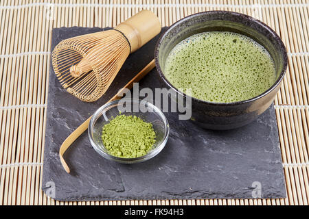 Poudre de thé vert matcha et fouet et cuillère et pour la préparation sur la plaque en pierre noir et blanc tapis de table en bambou Banque D'Images