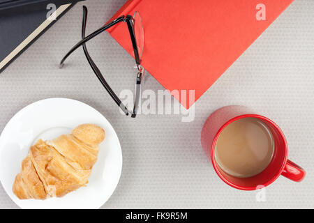 Voir ci-dessus d'un dessus de table d'un lecteur de prendre une pause café et un croissant Banque D'Images