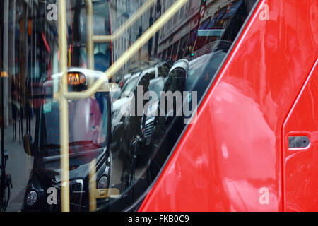 Un taxi noir et autre trafic reflète dans la fenêtre arrière d'un double decker bus de Londres. Banque D'Images