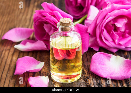 L'huile essentielle de Rose dans un flacon avec pétales de roses et sur planche de bois Banque D'Images