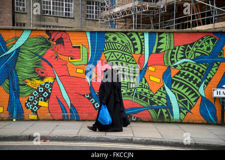 Le Hanbury Street, à côté de Brick Lane. Tower Hamlets. Deux femmes portant des voiles et manteaux noirs devant une murale colorée. Banque D'Images