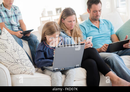 Famille avec deux enfants (6-7, 8-9) sitting on sofa using laptop, et tablettes numériques Banque D'Images