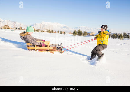 Enfants (8-9) en jouant avec la neige en traîneau Banque D'Images