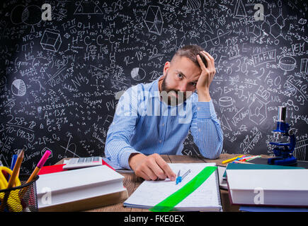 Contrarié enseignant à bureau, fournitures scolaires, holding head, blackboard Banque D'Images