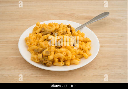 Vue latérale d'une fourchette insérée dans le macaroni au fromage avec des morceaux d'hamburger sur une plaque blanche au sommet d'une table en bois. Banque D'Images