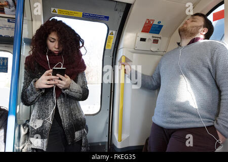 Un jeune homme et femme sur un london underground tube train d'écouter de la musique sur leur téléphone mobile, London UK Banque D'Images