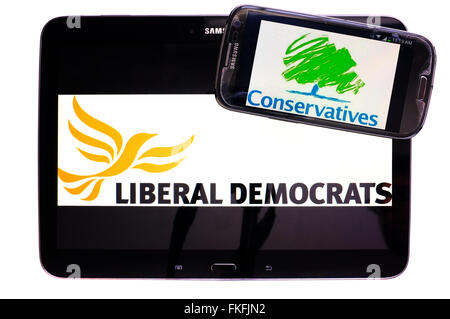 Une tablette avec les Libdem logo sur elle et un smartphone avec le logo du parti conservateur sur elle sur un fond blanc. Banque D'Images