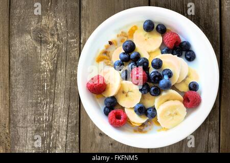 Céréales Petit déjeuner avec des bleuets, bananes et framboises sur un fond de bois rustique, overhead view Banque D'Images