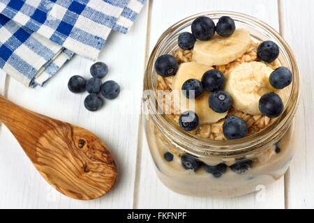 La nuit petit-déjeuner banane myrtille et d'avoine dans un pot Mason, avec cuillère de bois blanc sur Banque D'Images