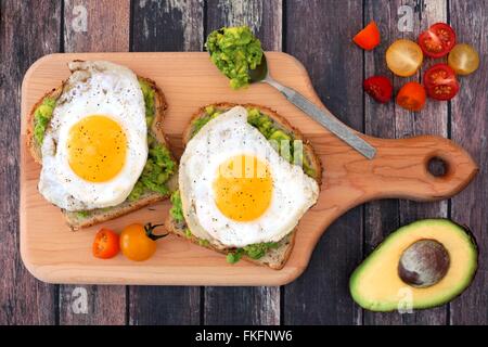 L'avocat, l'egg sandwiches ouverts sur pain de grains entiers avec des tomates on paddle board avec table en bois rustique Banque D'Images