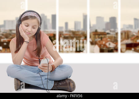 Une fille préadolescente écoutez de la musique avec son smartphone, assis en tailleur Banque D'Images