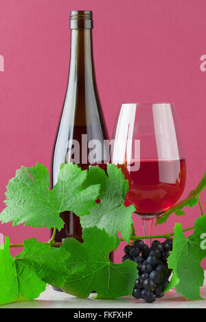 Bouteille de vin rouge et verre avec des raisins mûrs sur fond rose et de marbre Banque D'Images