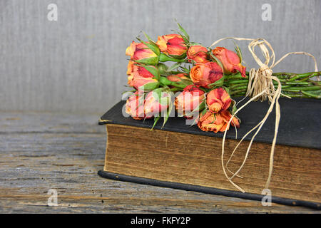 Bouquet de roses orange avec du raphia noeud sur livre ancien. Banque D'Images