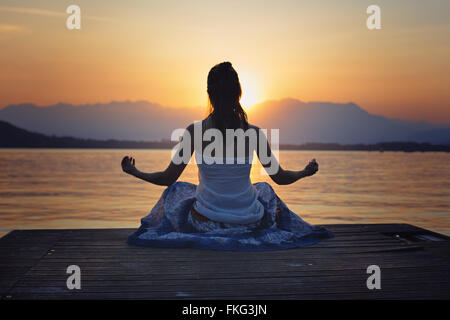 Femme silhouette devant le coucher du soleil sur le lac d'or colorés . Le yoga et la méditation Banque D'Images